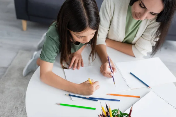 High angle view of brunette babysitter and kid drawing on paper — Stock Photo