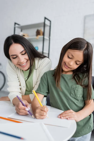 Happy babysitter and cheerful kid drawing on paper with colorful pencils - foto de stock