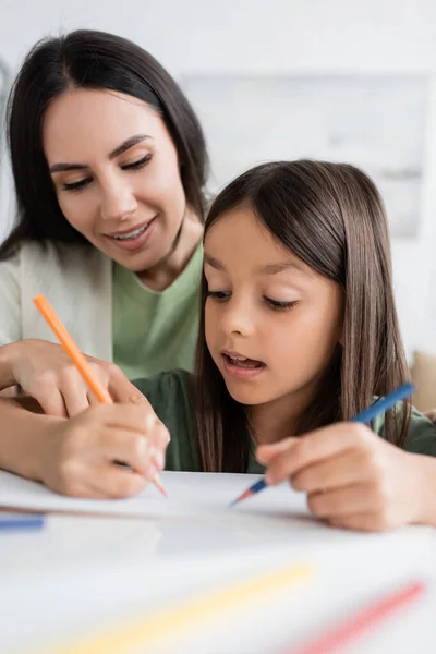 Happy babysitter looking at child drawing on paper with colorful pencils — Photo de stock