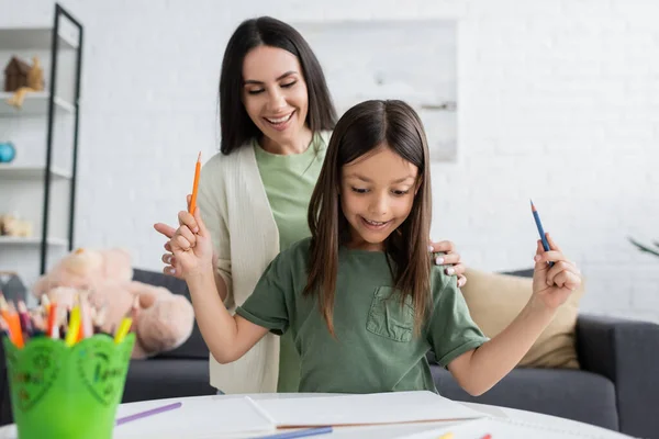 Babysitter felice guardando bambino felice che tiene matite colorate vicino alla carta — Foto stock