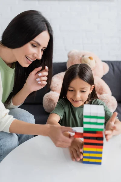 Happy babysitter playing wood blocks game with girl in living room - foto de stock
