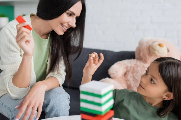 Joyeux baby-sitter jouer jeu de blocs de bois avec fille dans le salon — Photo de stock