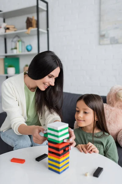 Happy babysitter playing wood blocks game with pleased girl in living room — Stock Photo