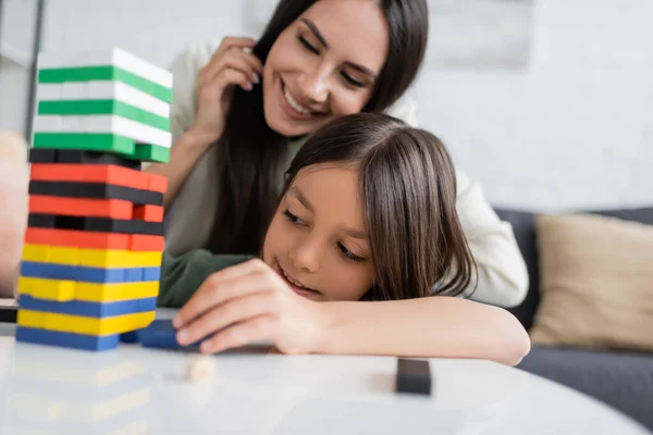 Baby-sitter heureux jouant tour en bois jeu avec fille heureuse dans le salon — Photo de stock