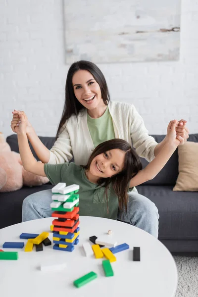 Babá feliz jogando jogo de torre de madeira com menina alegre na sala de estar — Fotografia de Stock