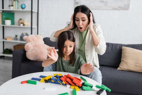 Chocado babá tocando cabeça perto chateado menina e coloridos blocos de madeira — Fotografia de Stock