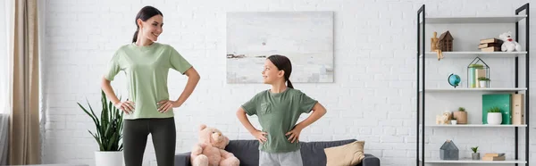 Child and babysitter training with hands on hips and smiling at each other, banner — Stockfoto