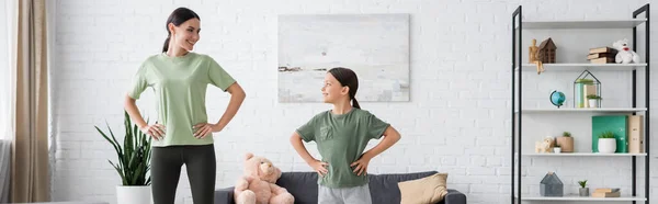 Entrenamiento del niño y de la niñera con las manos en las caderas y sonriendo el uno al otro, bandera - foto de stock