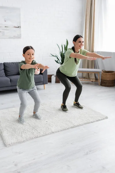 Full length of positive nanny and child doing sit ups with outstretched hands at home — Foto stock