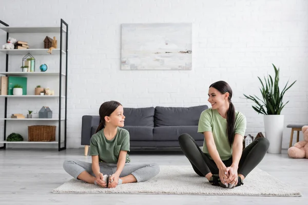 Girl and babysitter smiling at each other while sitting on carpet in fire log pose - foto de stock