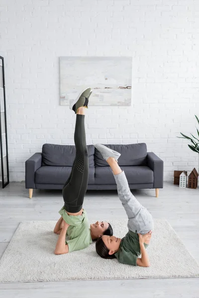 Glückliches Mädchen mit Babysitter-Training im unterstützten Schulterstand posiert auf Teppich im Wohnzimmer — Stockfoto