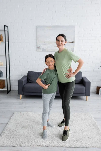 Full length of happy nanny and child in sportswear embracing and looking at camera — Stock Photo