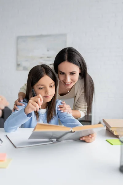 Cheerful nanny and child looking at textbook together — Foto stock
