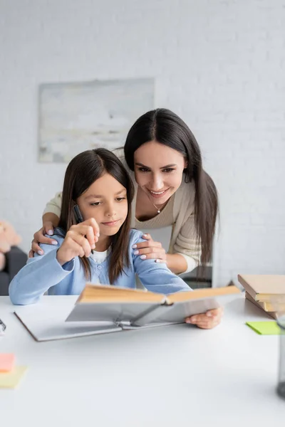 Cheerful nanny and child looking at textbook together — Fotografia de Stock