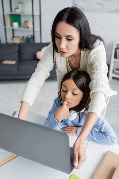 Babysitter looking at laptop near thoughtful girl during online lesson — Photo de stock