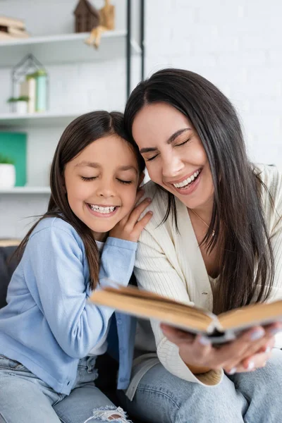 Glückliches Mädchen und Kindermädchen mit geschlossenen Augen lächelnd in der Nähe von Buch zu Hause — Stockfoto