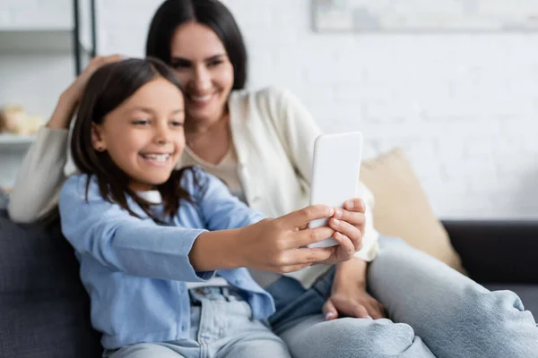 Menina feliz tomando selfie no telefone móvel com babá no fundo embaçado — Fotografia de Stock