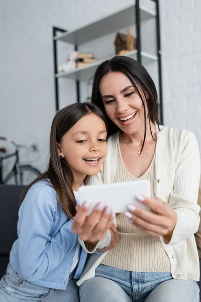 Child and nanny smiling near blurred smartphone during video call at home — Stock Photo