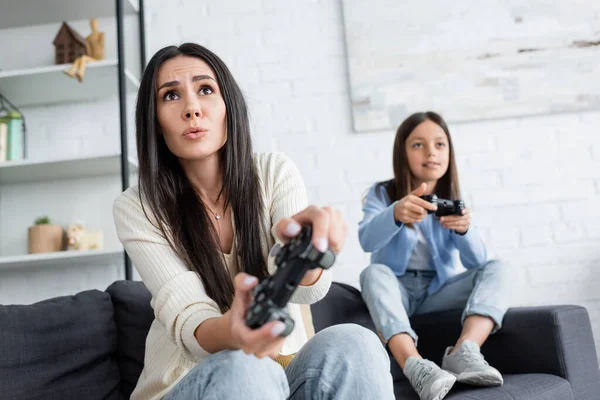 KYIV, UKRAINE - MAY 23, 2022: concentrated nanny gaming near blurred girl on sofa at home - foto de stock