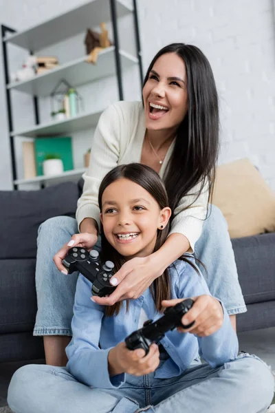 KYIV, UKRAINE - MAY 23, 2022: excited nanny and child playing video game with joysticks at home — Stockfoto