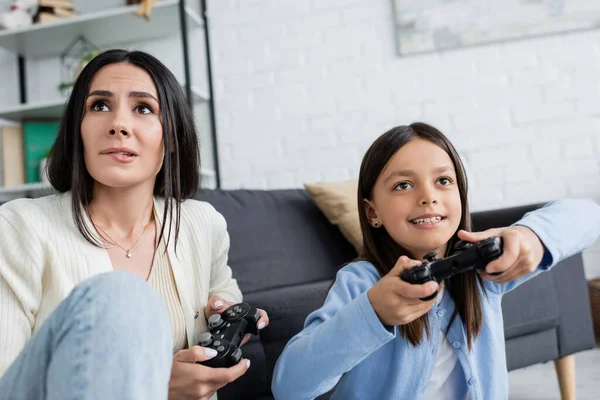 KYIV, UKRAINE - MAY 23, 2022: worried babysitter biting lip while gaming with cheerful girl at home - foto de stock