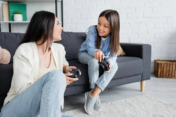 KYIV, UKRAINE - 23 MAI 2022 : fille heureuse et baby-sitter avec des joysticks se regardant dans le salon — Photo de stock