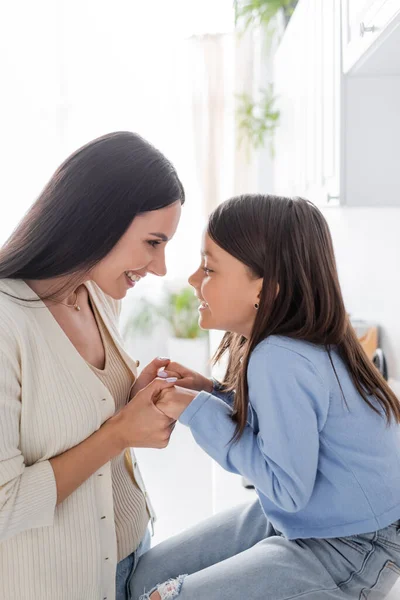 Seitenansicht des Babysitters hält Händchen mit Mädchen, während er in der Küche von Angesicht zu Angesicht lächelt — Stockfoto