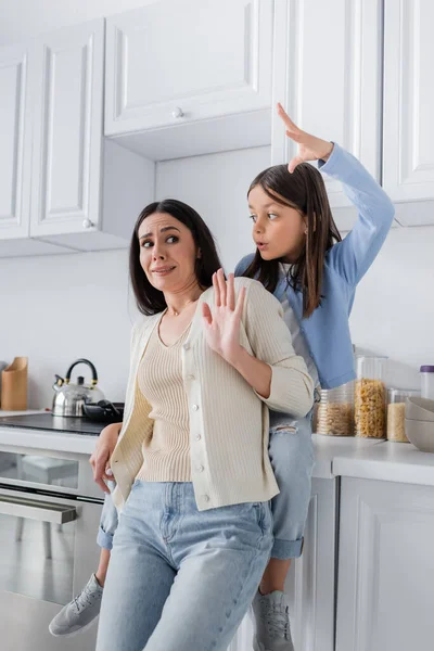 Girl sitting on worktop in kitchen and scaring nanny — Stock Photo