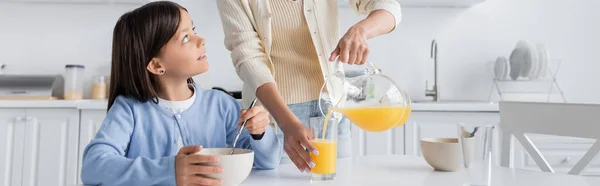 Chica con tazón mirando niñera verter jugo de naranja fresca, pancarta - foto de stock