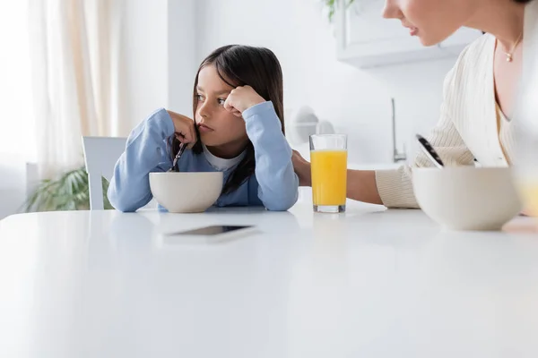 Offeso ragazza guardando lontano vicino a colazione e tata offuscata in cucina — Foto stock