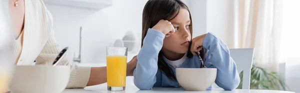 Расстроенный ребенок сидит рядом с няней и смотрит в сторону во время завтрака, баннер — стоковое фото
