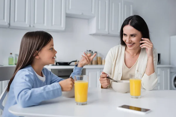 Mädchen im Gespräch mit glücklichen Kindermädchen in der Nähe von Schüsseln mit Frühstück und frischem Orangensaft — Stockfoto