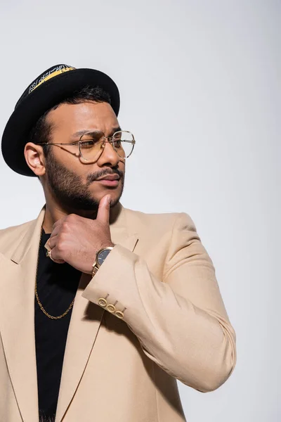 Elegante artista indio de hip hop en sombrero de sombrero fedora y anteojos mirando hacia otro lado aislado en gris - foto de stock