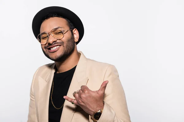 Feliz artista indio de hip hop en sombrero fedora y gafas que muestran llámame gesto aislado en gris - foto de stock