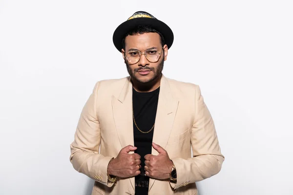 Indian hip hop singer in fedora hat and eyeglasses adjusting blazer isolated on grey — Photo de stock