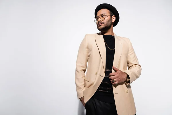 Vue à angle bas de l'artiste hip hop indien élégant en chapeau fedora et lunettes debout avec la main dans la poche sur gris — Photo de stock