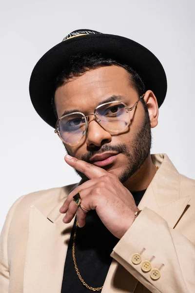 Portrait of stylish indian hip hop performer in fedora hat and eyeglasses isolated on grey - foto de stock