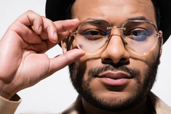 Close up of bearded indian hip hop performer in fedora hat adjusting eyeglasses isolated on grey — Fotografia de Stock