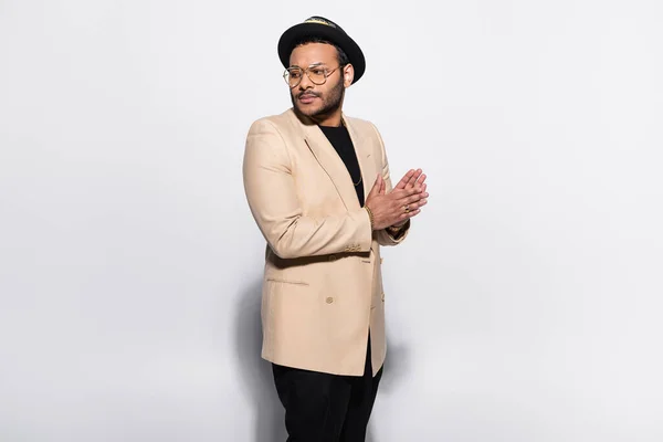 Stylish indian hip hop performer in fedora hat and eyeglasses standing and looking away isolated on grey — Stockfoto