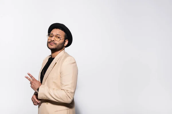 Stylish indian rapper in fedora hat and eyeglasses showing peace sign isolated on grey — Stock Photo