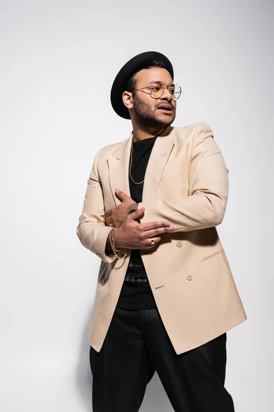 Cantante de hip hop indio de moda en sombrero fedora y gafas de pie en gris - foto de stock