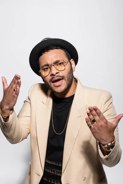 Eastern hip hop singer in fedora hat and eyeglasses singing while gesturing on grey — Stock Photo