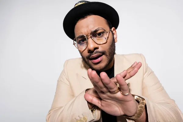Östliche Hip-Hop-Performerin mit Fedora-Hut und Brille, die Stop-Geste isoliert auf grau zeigt — Stockfoto