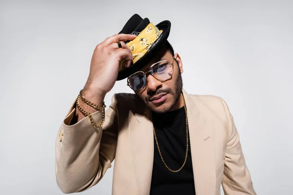 Eastern hip hop performer in eyeglasses holding fedora hat and looking at camera isolated on grey — Stock Photo