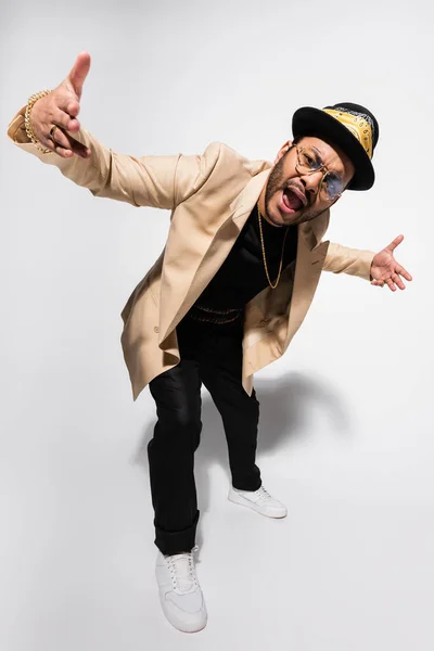 Volle Länge des östlichen Hip-Hop-Performers mit Fedora-Hut und Brille, der auf grau singt — Stockfoto