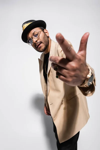 Bearded eastern hip hop performer in fedora hat and eyeglasses gesturing on grey — Stock Photo