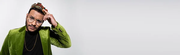 Indian hip hop performer in green velvet blazer adjusting crown isolated on grey, banner — Stock Photo