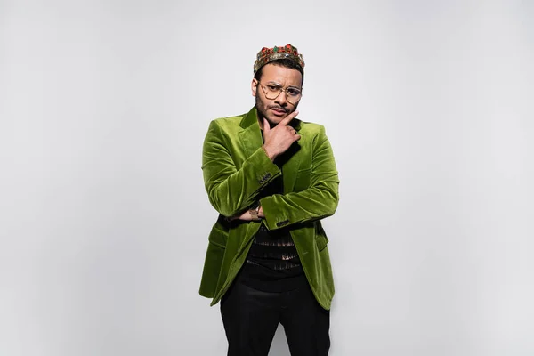 Pensive eastern hip hop performer in green velvet blazer and crown isolated on grey — Stock Photo