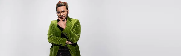 Задумчивый восточный хип-хоп исполнитель в зеленом бархатном пиджаке и корона изолированы на сером, баннер — стоковое фото