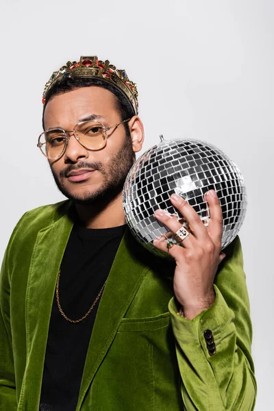 Artista indio de hip hop en chaqueta de terciopelo verde y corona sosteniendo bola disco aislada en gris - foto de stock